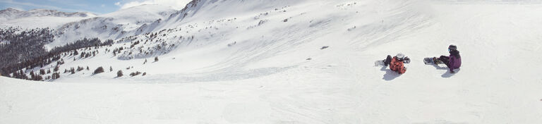 Snowboarders in open snow field mid-run
