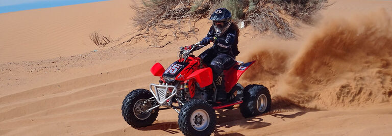 Erika riding a red 4 wheeler in desert sand