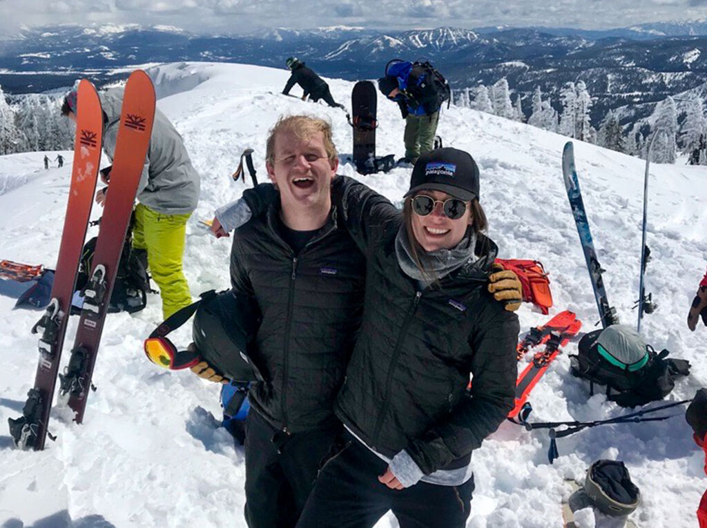 Clare and her partner smiling on a mountain  ridge with their ski gear