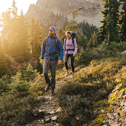 man and woman outside hiking with packs on a trail through the mountains