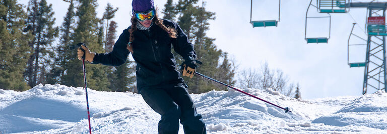 Erika skiing moguls under a ski lift on a sunny day