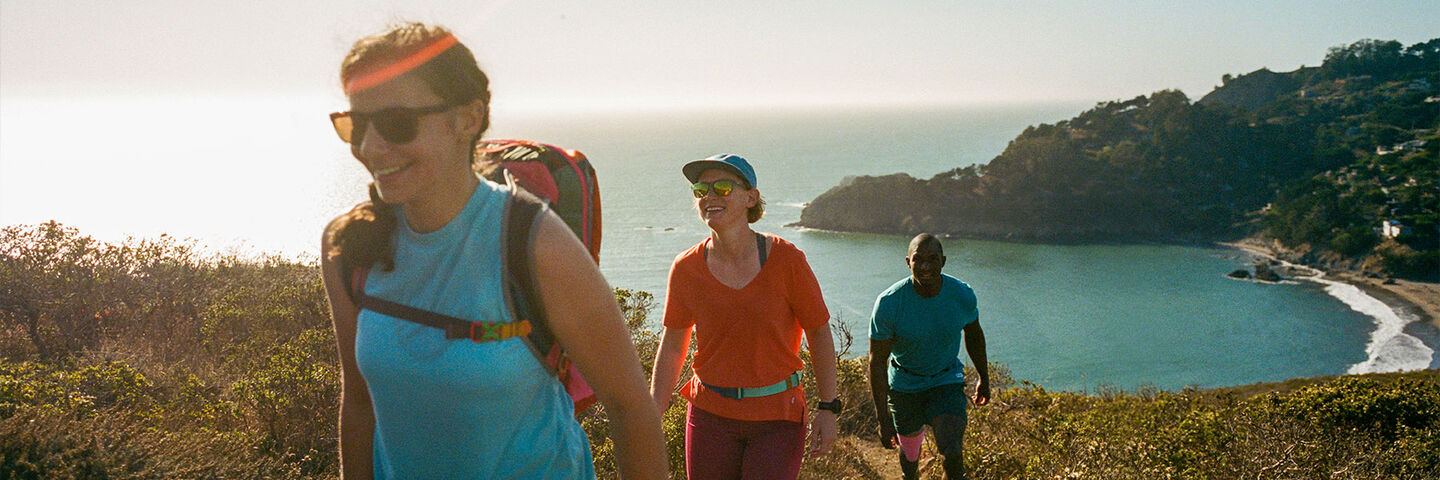 three people hiking on the coast line wearing cotopaxi