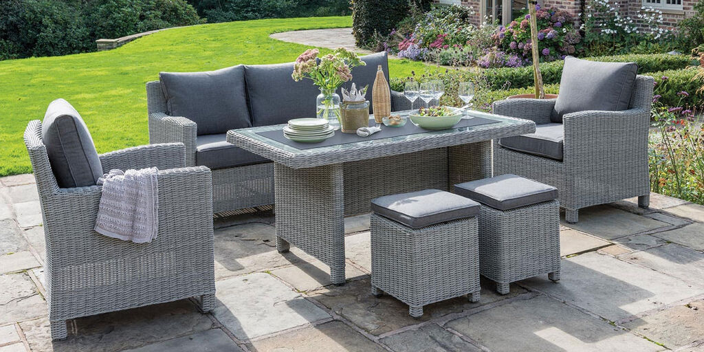 woven outdoor lounge set of chairs, sofa and ottomans with cushions with chat table on stone patio