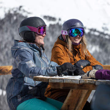 two women in ski gear sitting at a picnic table
