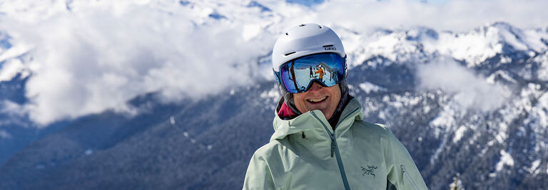 Tracy in ski gear smiling in front of mountains 