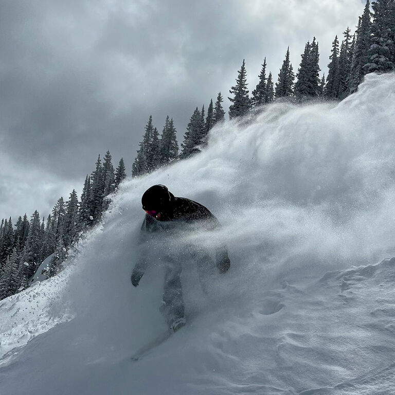 Jake J spraying a cloud of powder while snowboarding