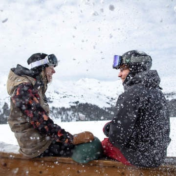 two skiers sitting on a railing with mountain view