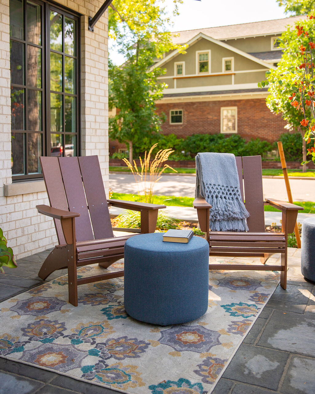 Two brown Adirondack patio chairs made of recycled materials by Polywood accented by a pool stool on an outdoor rug