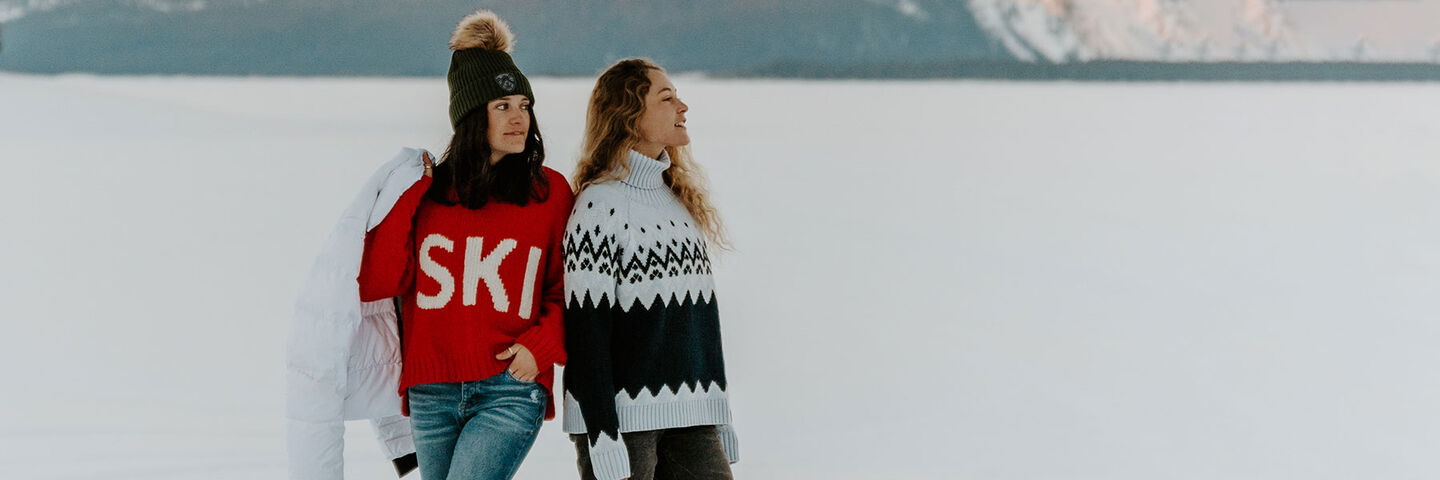 Two women standing in a snowy field wearing krimson klover sweaters
