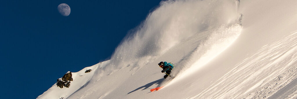 Skier making a pow turn on a steep mountain face