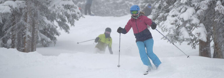 Charlotte skiing through trees on a powder day